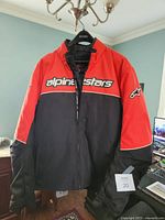 Front view of red/black Alpinestars motorcycle jacket on hanger