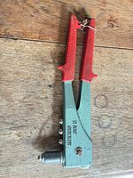 Full view of rivet gun showing green body, red handles, nosepieces in side storage