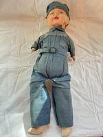 Full view of doll in blue jumpsuit and cap laid flat