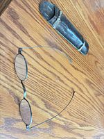 Eyeglasses unfolded beside metal case on wood surface