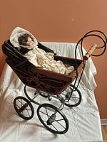 Side view of wooden and metal doll carriage with doll inside