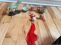 overview showing jade horse on stand, three porcelain cups, large red tassel, small tassel