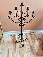 Full view of black wrought iron floor candelabra with scrollwork and tripod base