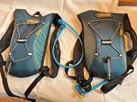 Two CamelBak hydration packs side by side showing front views and drinking tube