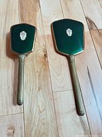 Front view of two hand mirrors showing green enamel backs and brass handles