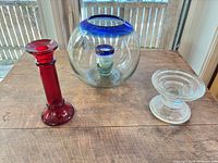 All three glass pieces together: red candlestick, globe vase with blue rim, clear pedestal bowl