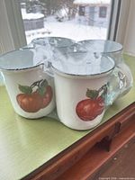 Four shrink-wrapped ceramic mugs with apple design on side