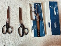 Overview of three scissors; two black-handled out of box, one chrome-handled in box