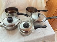 All five saucepans displayed with three lids visible