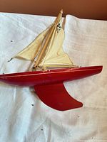 Side profile of red wooden hull sailboat with cream cloth sails and fixed keel
