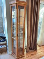 Full view of cabinet showing wood frame, glass panels, overall height and narrow footprint