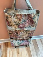 Front view of floral tapestry rolling shopping trolley bag showing pattern, handles and wheel base