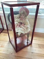 Full view of doll seated in chair within glass case