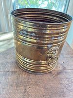 Front view of brass jardinière showing ribbed bands, lion-head handle, tarnish and verdigris