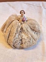 front view of porcelain half-doll pincushion showing lace skirt and figurine details