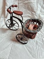 Full view of tricycle showing metal frame, three wheels, wood seat and grips, attached wicker basket