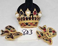 Front view of crown brooch and pair of bow earrings on white background