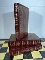 Three burgundy leather-bound books, one standing, showing front cover design