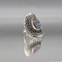 Front angled view of sterling silver filigree ring showing oval multicolor druzy stone and decorative border
