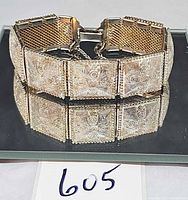 Full view of bracelet standing on mirrored surface showing front filigree panels