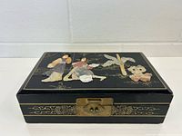 Closed jewelry box lid showing carved stone figures and brass latch