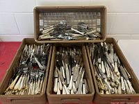 three brown plastic trays filled with stainless knives and forks
