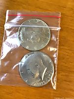 Both Kennedy half-dollar coins inside small plastic zip bag