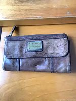 Front of wallet showing logo plate and exterior zip compartment