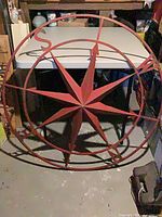 Full view of red metal compass rose leaning against table