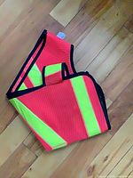 Folded fluorescent orange safety vest with reflective yellow stripes on wooden floor