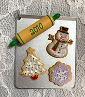 Front of silver miniature cookie sheet ornament with rolling pin and decorated cookie designs