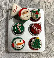 Front of silver cookie tray ornament showing six decorated holiday treats and 2010 tag
