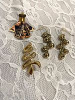 Front view of angel brooch, rhinestone tree brooch, and jingle bell earrings on lace background