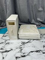 Stack of four shrink-wrapped beige fabric organizers beside one assembled unit showing window and handle