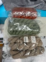 Three sealed packs of twisted cheesecloth runners in rust, green and taupe colours