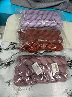 Three sealed packs of cheesecloth runners in lavender, rust orange and dusty mauve