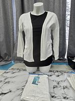 Mannequin displaying white ribbed cardigan with packaged unit on table