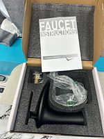 Box opened showing faucet body, hoses, mounting hardware and instructions