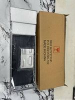 Sealed package containing three black shelves with white foam protectors beside the labeled master carton