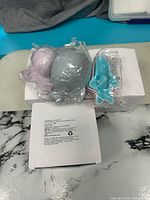 Three plastic bath toys (grey, lavender, turquoise) on top of sealed white box