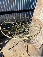 Full view of the round metal bistro table showing scrollwork base and glass top