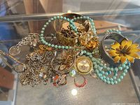 Pile of assorted costume jewelry including cuffs, beaded necklace, charm bracelet, pendant watch, rings, chains