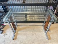 Front view showing glass top, metal frame, wood side panels, and wire shelf