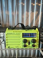 Front of lime green CR1009 emergency radio showing speaker grille, tuning display, knobs, and carry strap