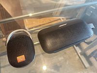 Bose and JBL portable Bluetooth speakers on glass surface