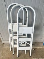 Two white folding step ladders leaning against wall