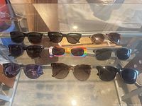 Nine pairs of sunglasses laid out on glass shelf