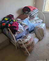 Daybed stacked with assorted blankets, quilts, comforters and packaged items