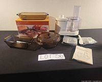 Group shot of amber bakeware set in front of box alongside Krups food processor with accessories and manual