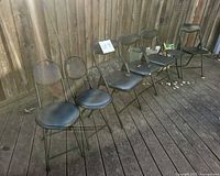 Row of six black metal folding chairs on deck